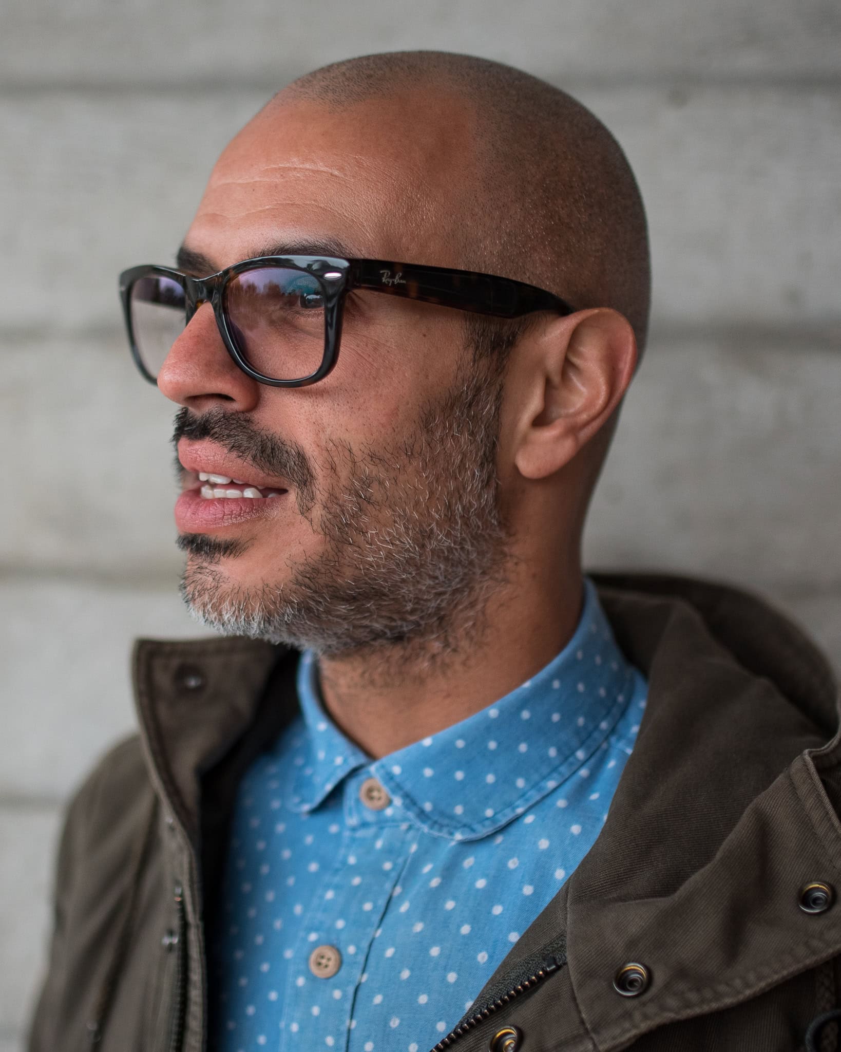 Cahit Ali, a man with glasses and a beard, wears a blue polka dot shirt and a green jacket in this London brand photography portrait.