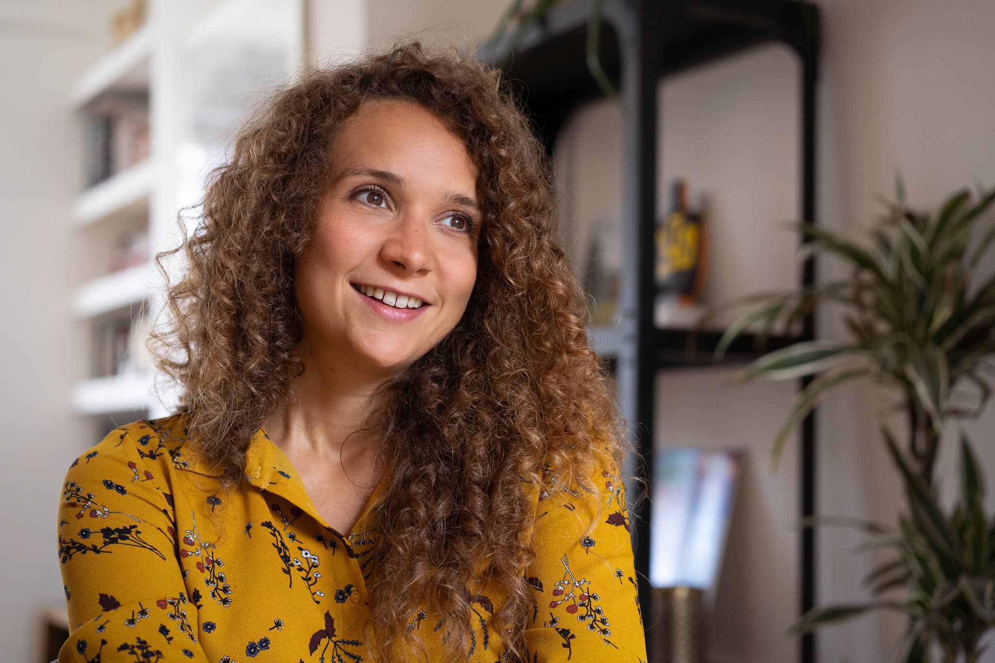 Lorraine Wilkes with curly hair smiling in a room with bookshelves and plants
