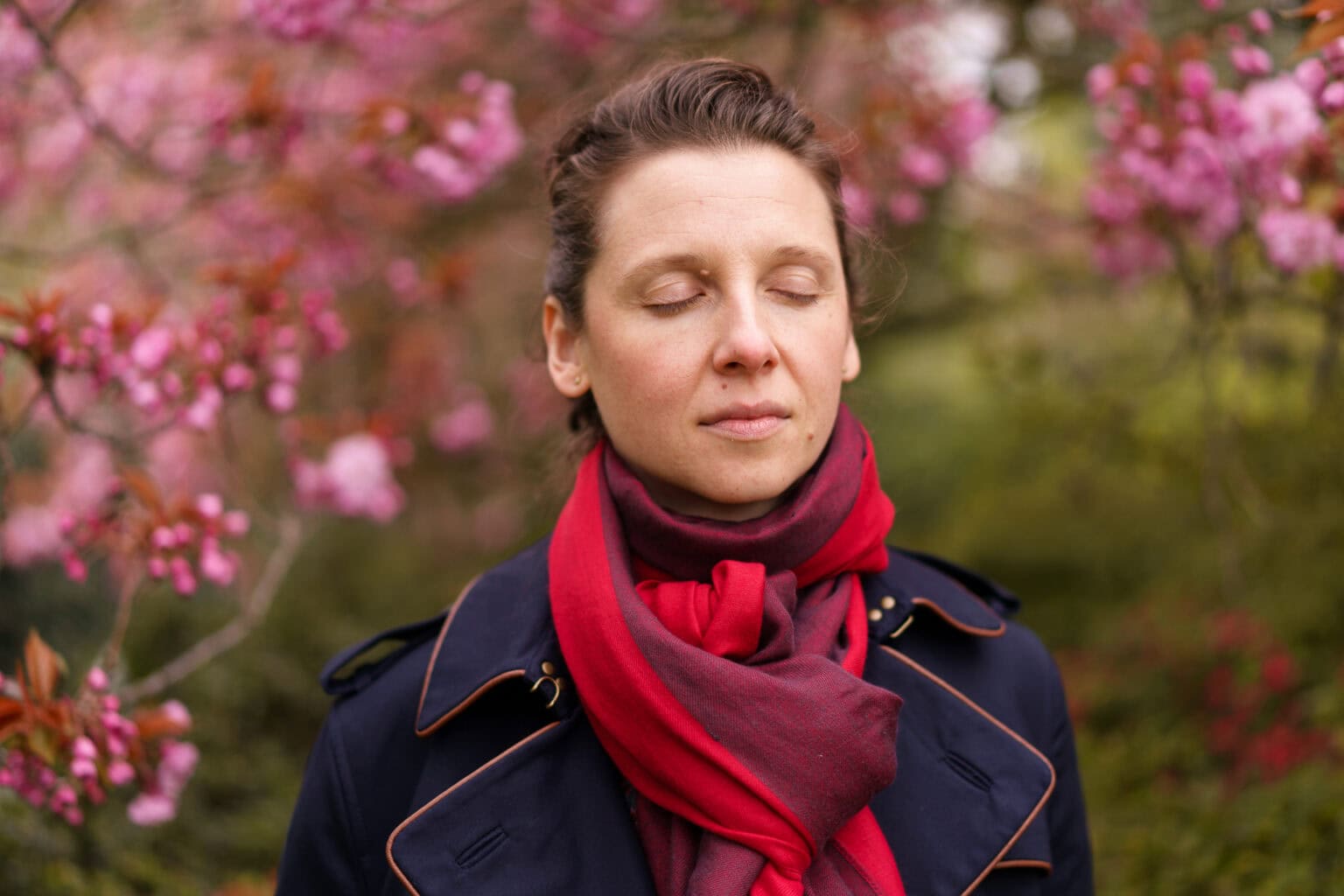 Moni Soos, a coach, in a thoughtful portrait with soft light and pink blossoms.
