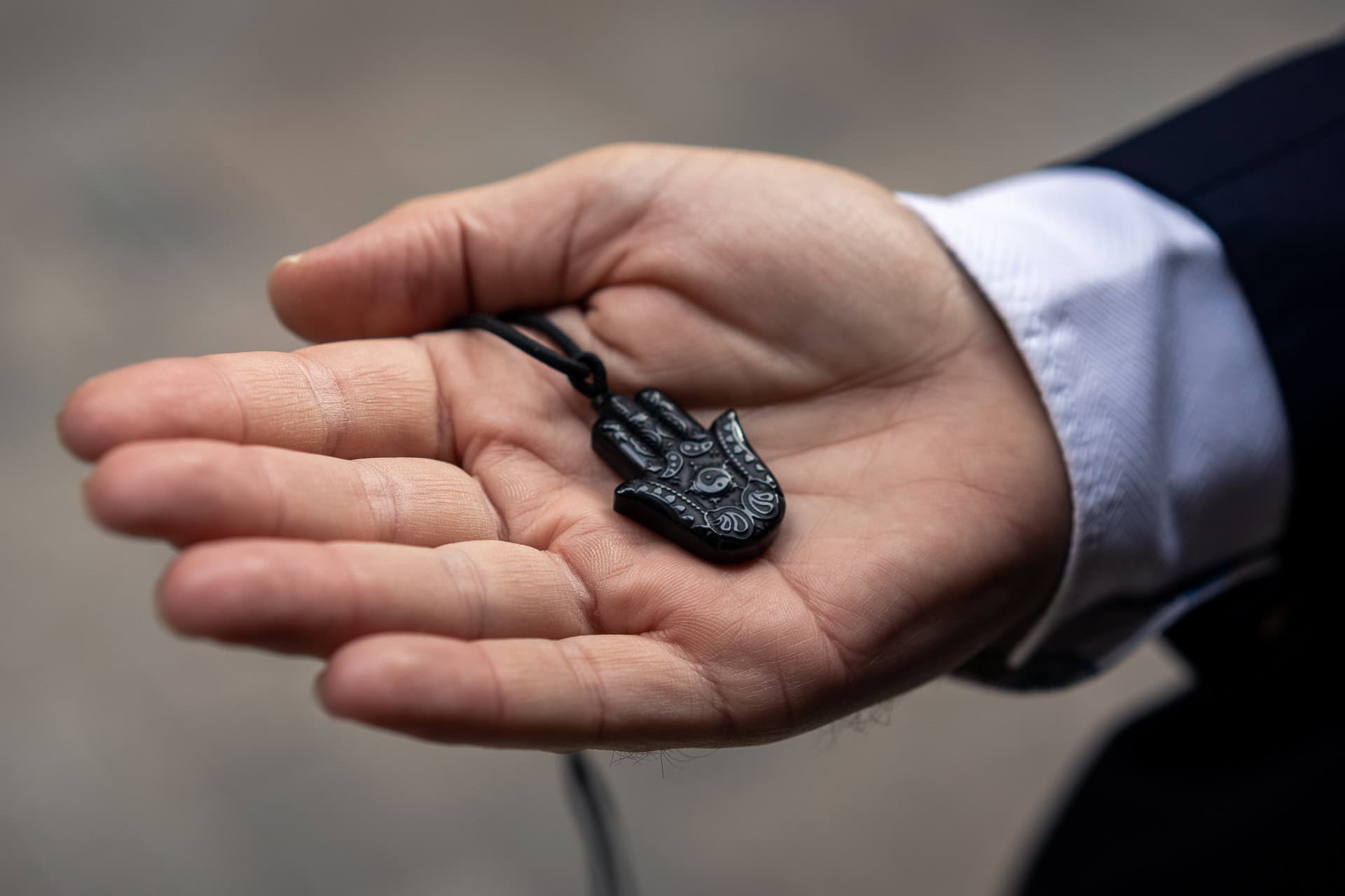 Zach Reynolds holds a black hamsa pendant, a symbol of protection, in his open palm.