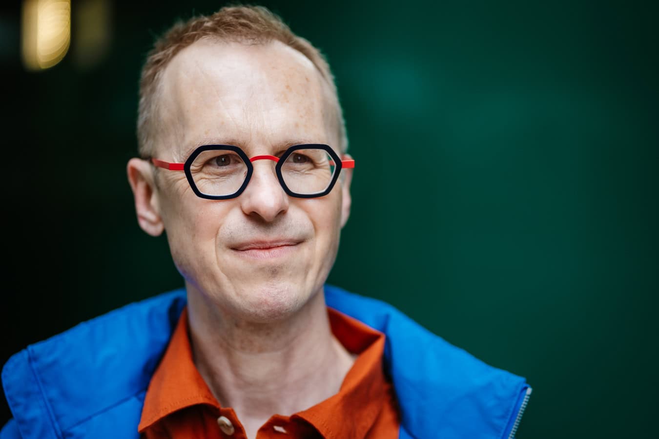 Richard Jones, a coach, wears distinctive red and black glasses and a blue jacket, captured in natural light.