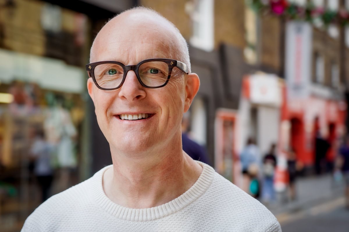 Jaap Parqui, a coach, smiles warmly in a sunlit London street, captured by a brand photographer.