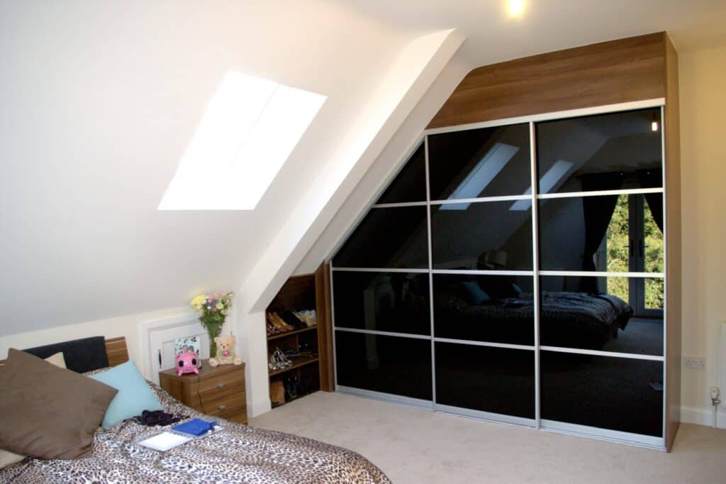 Contemporary fitted wardrobe with mirrored sliding doors in an attic bedroom setting.