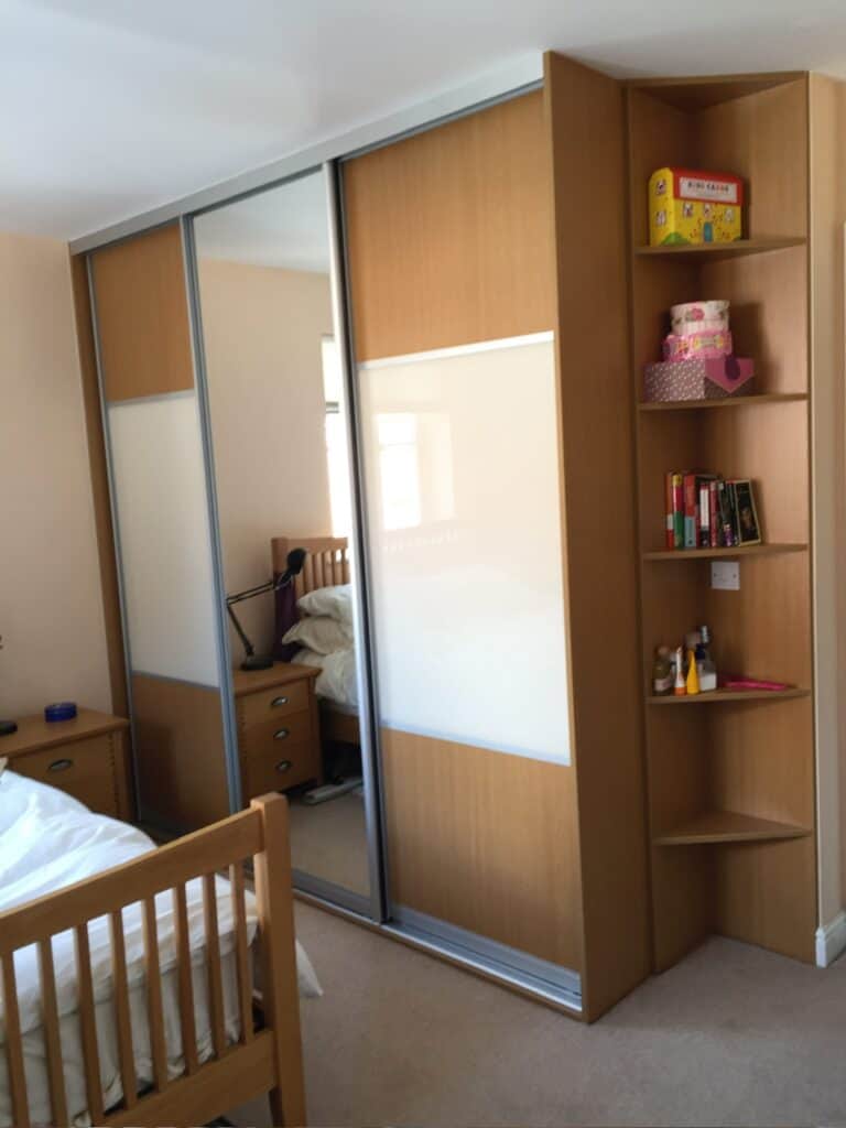 Custom-made fitted wardrobe with sliding doors and integrated shelving units for optimal bedroom storage.