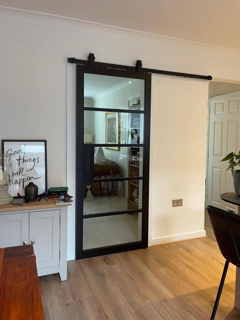 Black aluminium sliding barn door with glass panels, designed by Made 2 Measure Interiors, enhancing interior style and space.