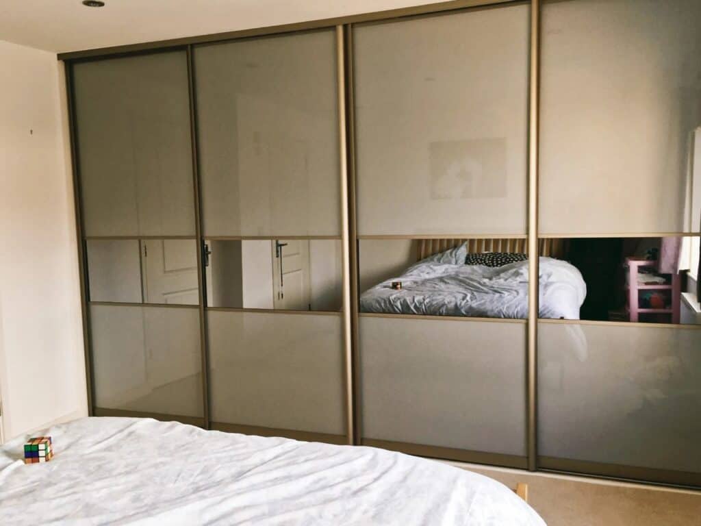Bespoke sliding wardrobe with mirrored panels, custom-made to fit stylish interiors.