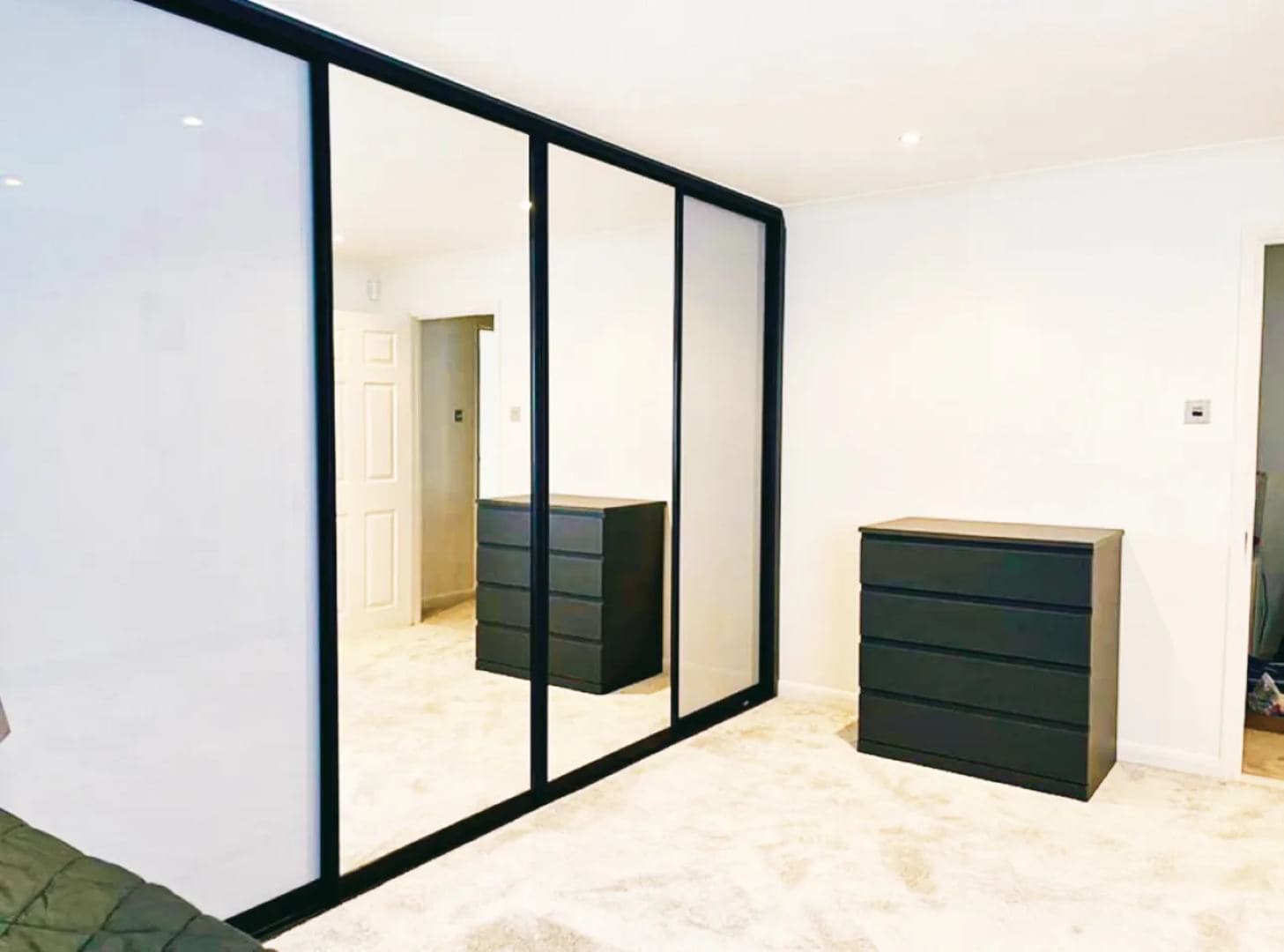 Sleek black-framed sliding wardrobe with mirrored doors enhances modern interior design.