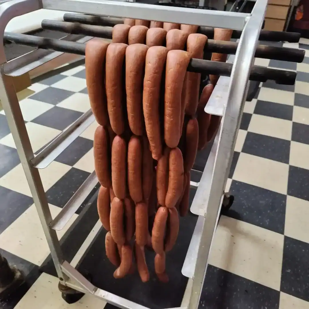 Fresh hot dogs hanging on a food cart in a market or street setting.