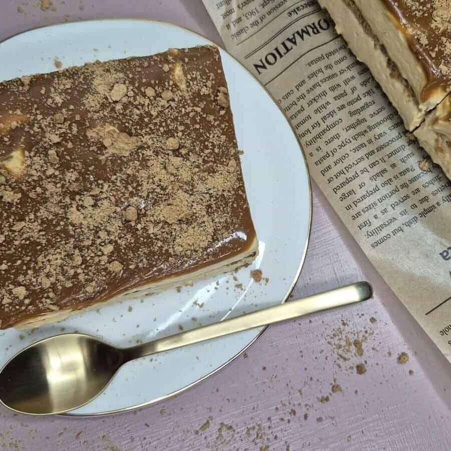 Caramel biscuit cake topped with crushed biscuits on a white plate, with one slice cut and served beside it