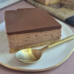 Square slice of no-bake Nutella chocolate bar with a biscuit base and smooth chocolate topping on a plate with a spoon.