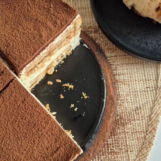 Whole no-bake Nutella biscuit cake dusted with cocoa, with one slice cut out to show the layers.