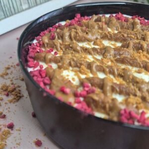 No-bake viral Japanese cheesecake in a black dish with Greek yogurt, coffee-dipped Lotus Biscoff biscuits, melted Biscoff spread, and pink crumb topping