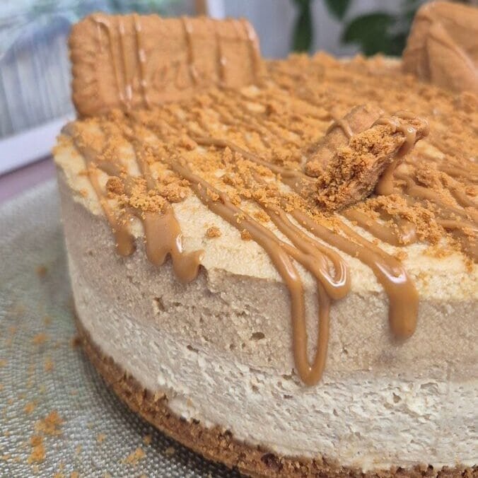 Whole Lotus Biscoff cake topped with crushed biscuits, Biscoff drizzle, and biscuit halves standing upright on top.