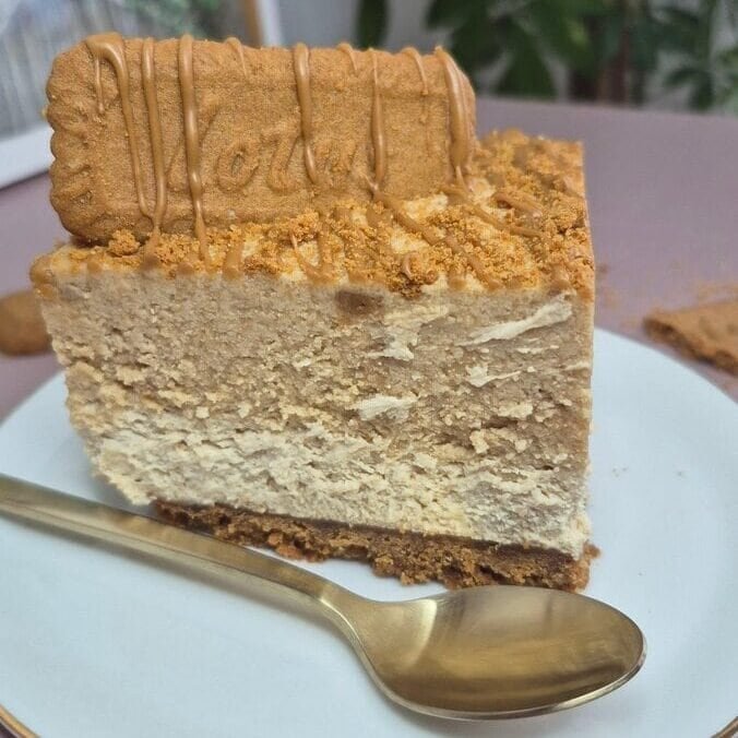 Slice of Lotus Biscoff cake with a biscuit crumb topping on a white plate, with a gold spoon beside it.