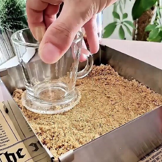 Hand pressing a graham cracker crust into a glass cup for dessert.