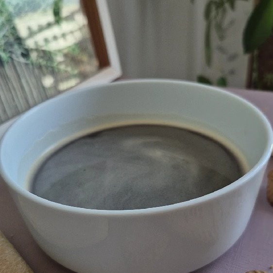 Rich, dark coffee in a white cup with a cozy indoor background.