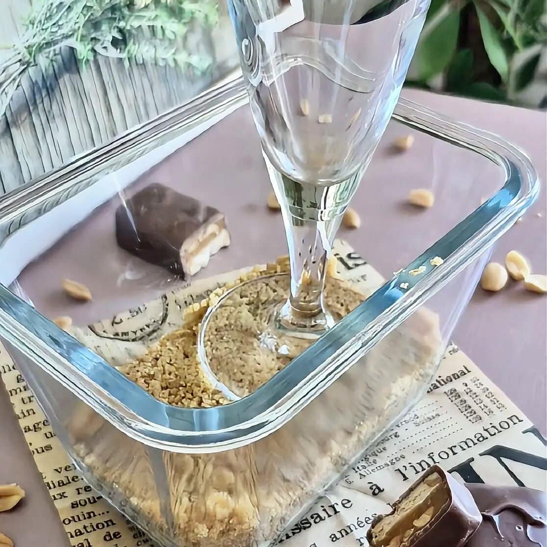 Close-up of a glass dessert cup with crushed cookies and chocolate, captured inside a glass display case.