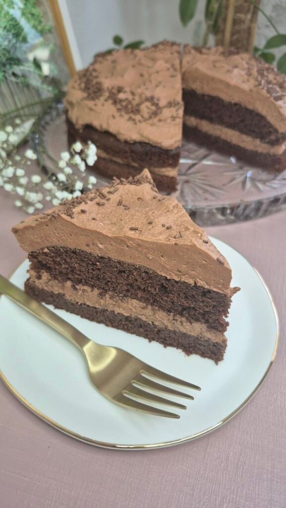 Slice of Matilda chocolate cake with whipped chocolate ganache filling on a white plate, with the rest of the cake in the background.