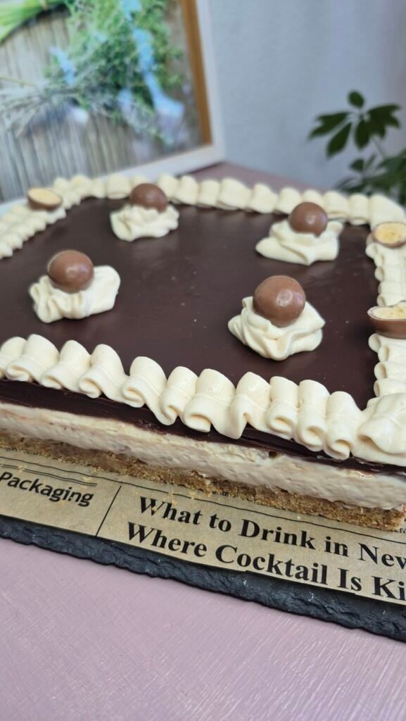 Whole no-bake chocolate ganache cheesecake in a square pan, topped with whipped cream rosettes and chocolate balls.