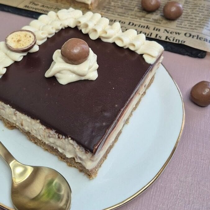 Square slices of no-bake chocolate ganache cheesecake topped with small whipped cream swirls, served on a white plate.
