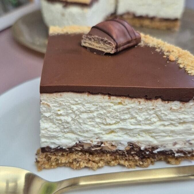 Close-up of a layered Nutella Kinder Bueno cake slice with crunchy biscuit crust, mascarpone cream filling, and Nutella topping