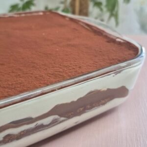 Whole hot chocolate tiramisu layered in a glass baking dish, dusted with cocoa