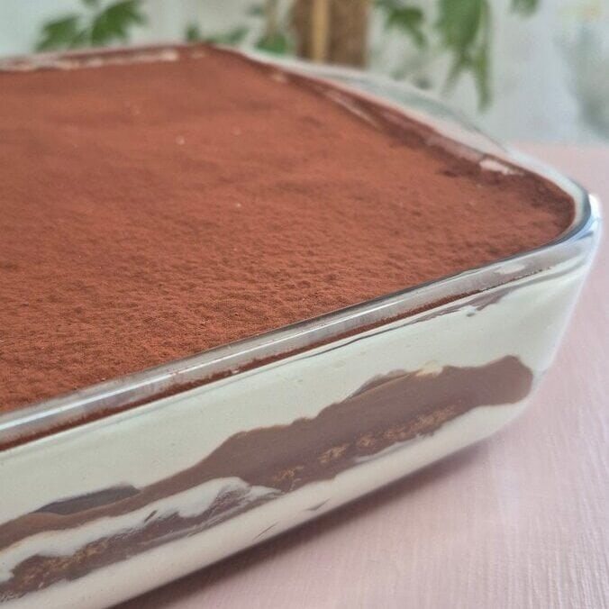 Whole hot chocolate tiramisu layered in a glass baking dish, dusted with cocoa