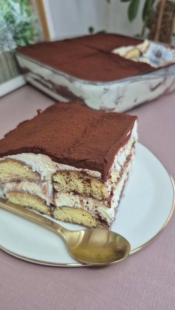 Slice of hot chocolate tiramisu on a plate with the full tiramisu in the background