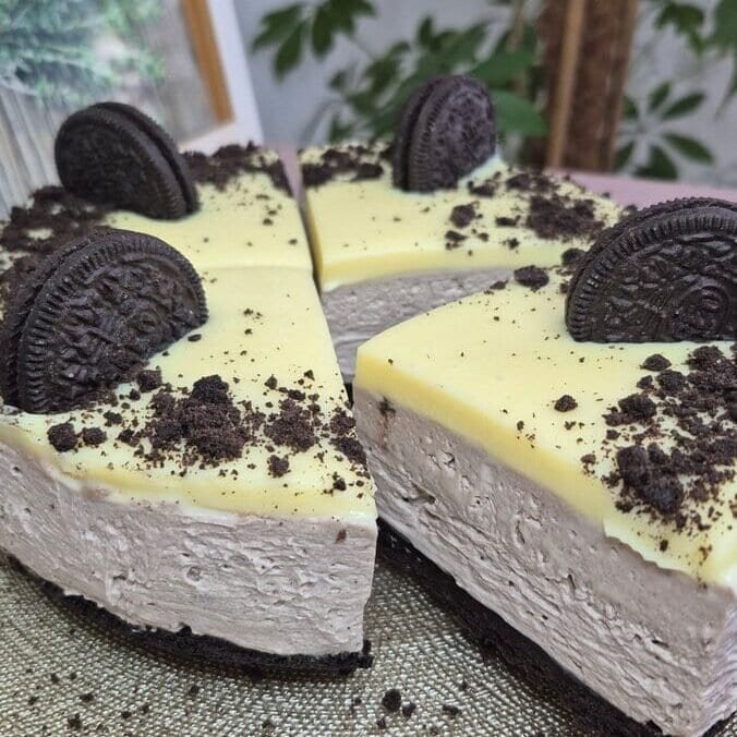Whole no-bake Oreo cake with a slice cut out, topped with white chocolate ganache and Oreo cookie crumbs.