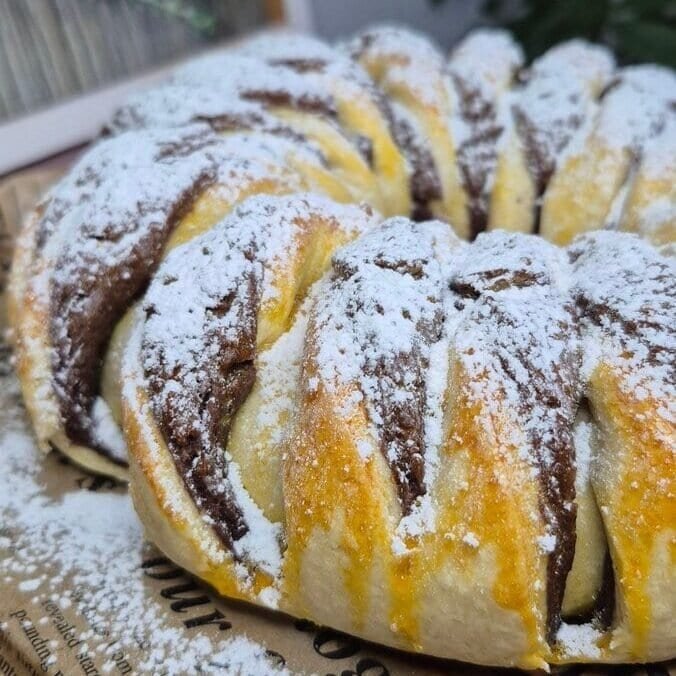 Whole Nutella bread roll with cocoa swirl, dusted with powdered sugar on a serving board.