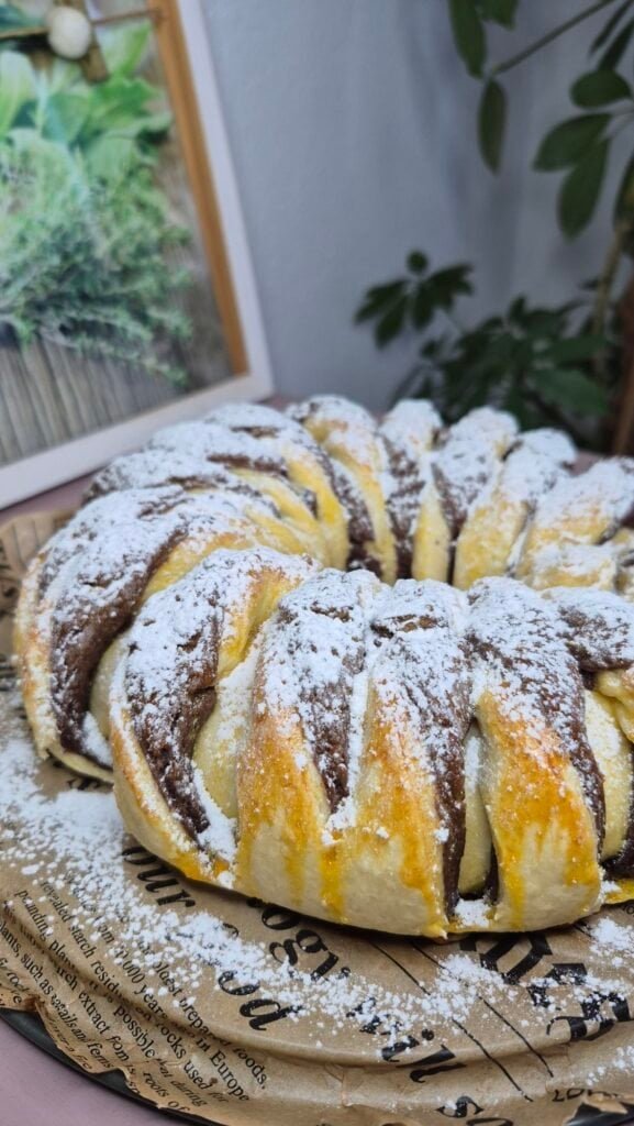 Whole Nutella bread roll with cocoa swirl, dusted with powdered sugar on a patterned plate.