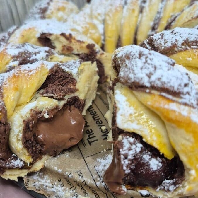 Sliced Nutella bread roll with cocoa swirl and chocolate chips, dusted with powdered sugar on a plate.