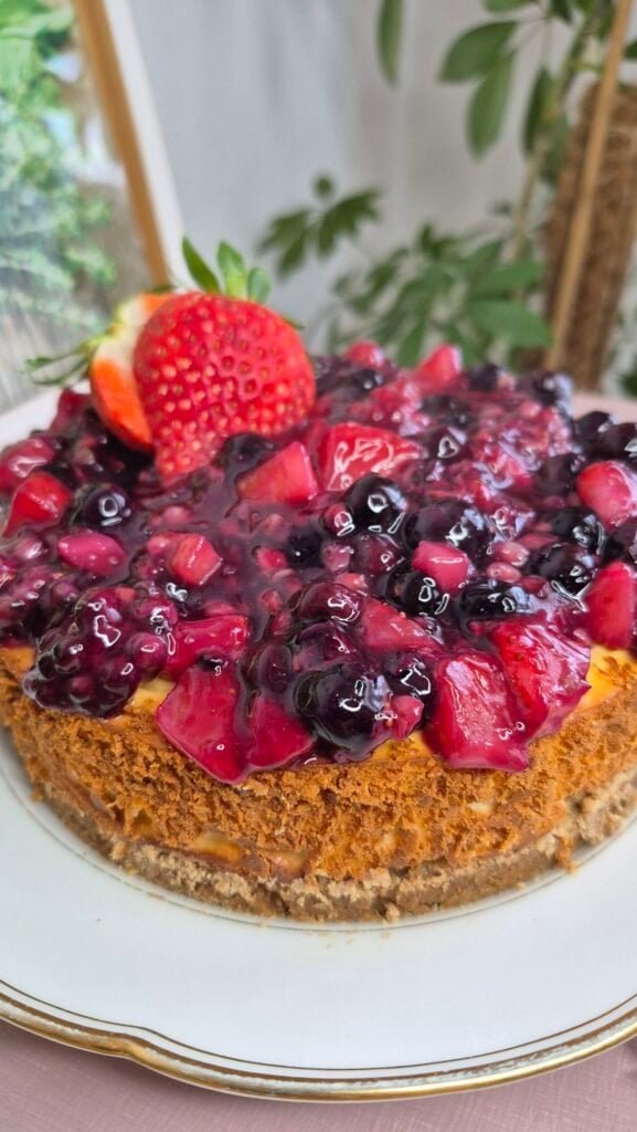 Baked ricotta cheesecake with glossy mixed berry topping and strawberries on a digestive biscuit crust