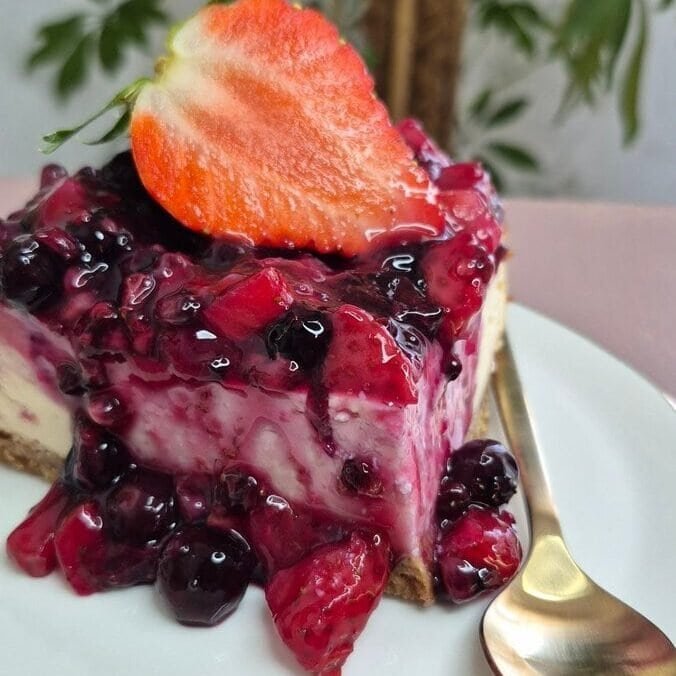Homemade ricotta cheesecake slice topped with cooked mixed berries, served on a white plate