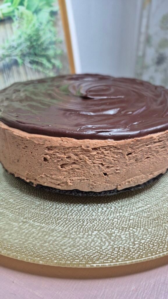 Whole no-bake Oreo cheesecake with dark chocolate ganache topping on a plate.
