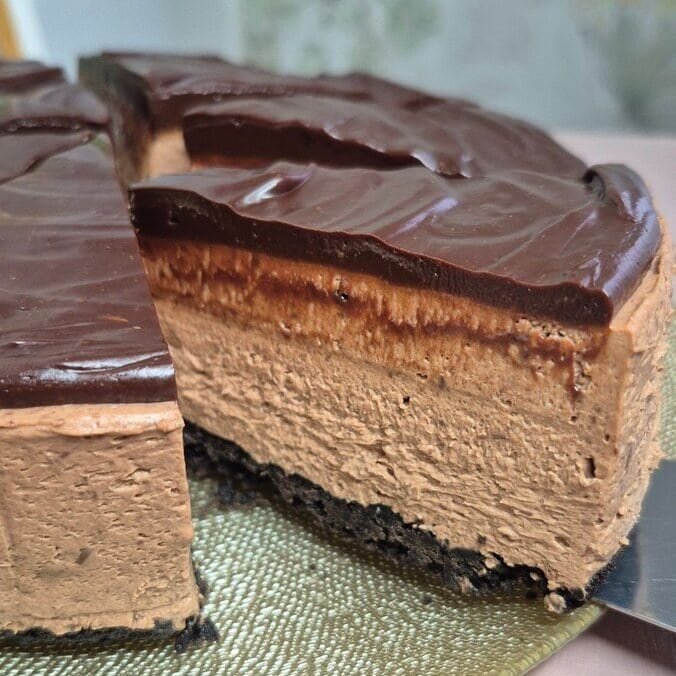 Side view of a no-bake Oreo cheesecake slice with dark chocolate ganache and cookie crust.
