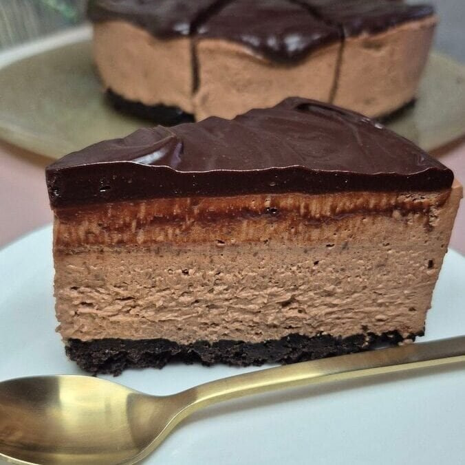 Slice of no-bake Oreo cheesecake with dark chocolate ganache on a white plate.
