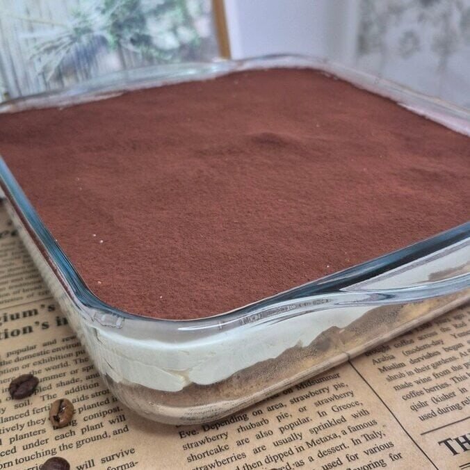 Whole Nutella tiramisu in a glass baking dish, topped with a thick layer of cocoa powder.