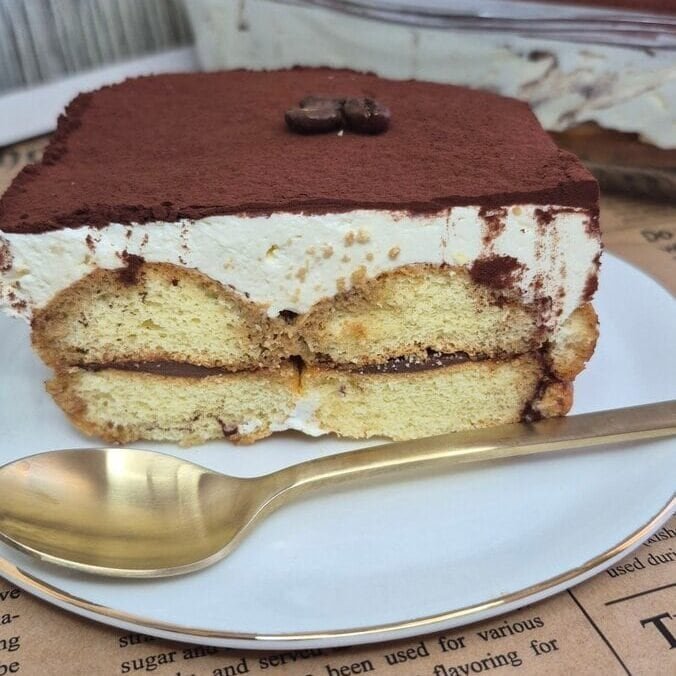 Slice of Nutella tiramisu with Savoiardi ladyfingers, mascarpone cream, and cocoa topping in a glass dish.