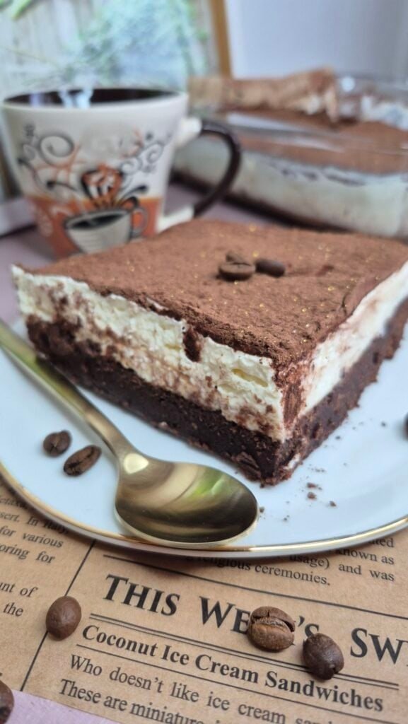 Slice of brownie tiramisu with a coffee-soaked chocolate brownie base, mascarpone cream layer, and cocoa powder topping on a plate.