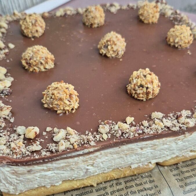 Whole no-bake Giotto cake in a square pan, topped with hazelnut milk chocolate ganache and decorated with Giotto balls.