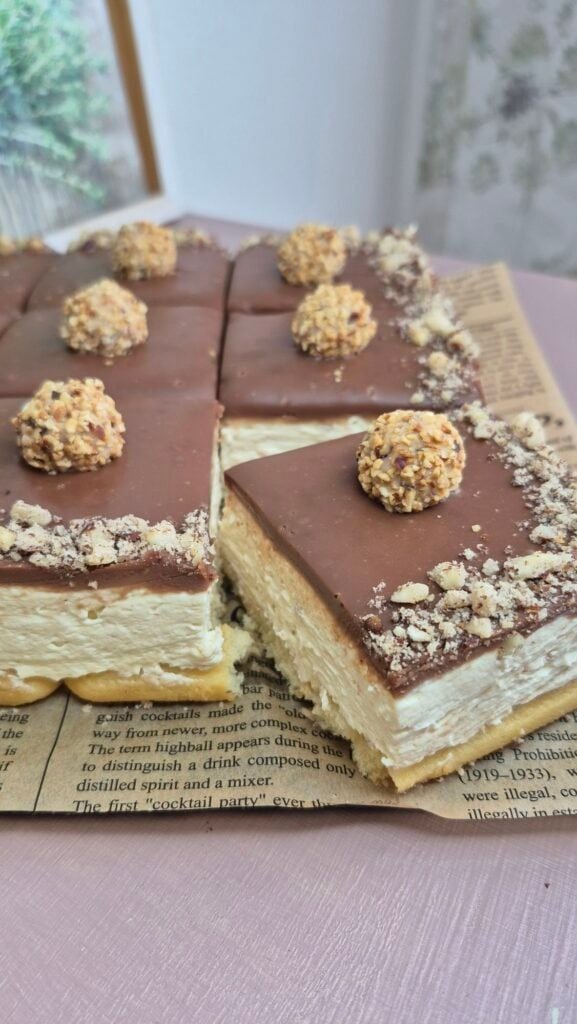 Square no-bake Giotto cake with a slice cut out, topped with hazelnut milk chocolate ganache and decorated with Giotto balls.