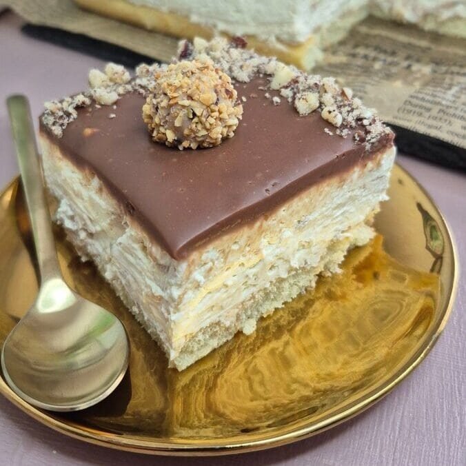 Slice of no-bake Giotto cake with milk-dipped ladyfingers, mascarpone cream filling, and hazelnut milk chocolate topping on a gold plate.