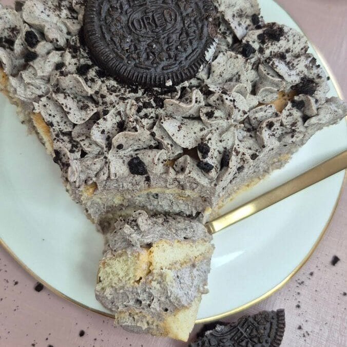Square slice of Oreo tiramisu topped with a whole Oreo cookie and crushed crumbs on a plate