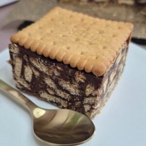 Slice of 3-ingredient mozaic cake (Petit Beurre biscuit cake) with chocolate ganache mosaic, served on a plate.