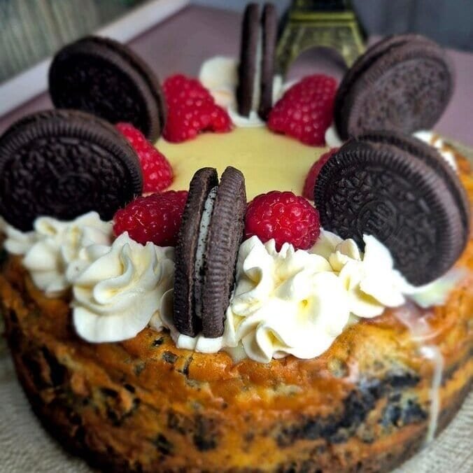 Whole Oreo cheesecake topped with whipped cream, raspberries, and Oreo cookies.