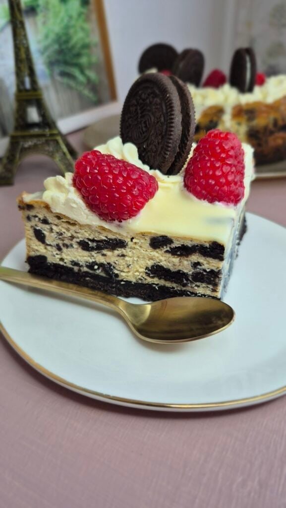 Slice of Oreo cheesecake with raspberries and an Oreo cookie on top.