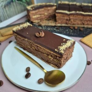 Slice of no-bake chocolate biscuit cake with creamy chocolate filling and glossy chocolate topping on a white plate