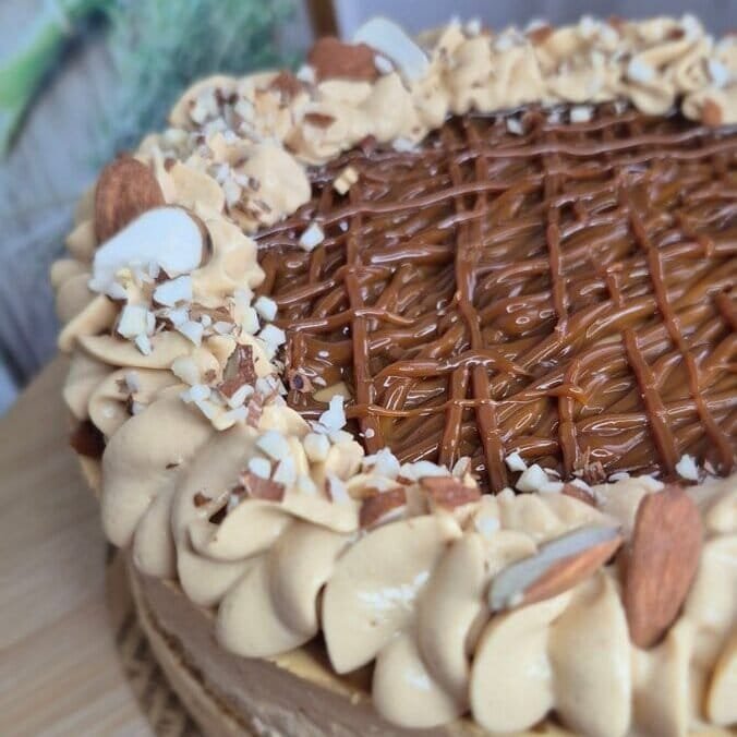 Baked cake with dulce de leche and mascarpone cream topped with piped cream, chopped nuts, and a chocolate decoration.