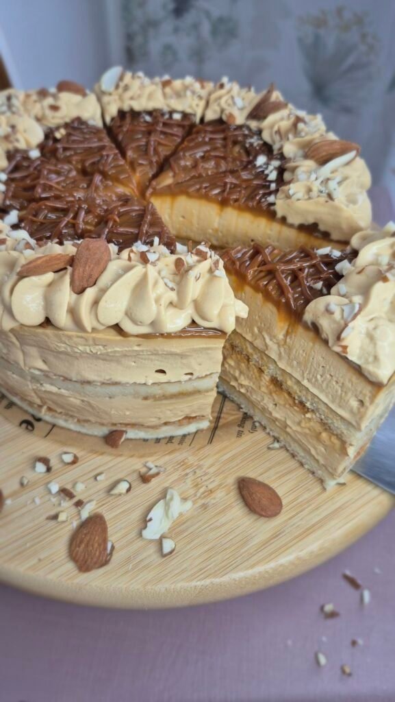 Baked cake with dulce de leche and mascarpone cream topped with piped cream, chopped nuts, and chocolate shavings.